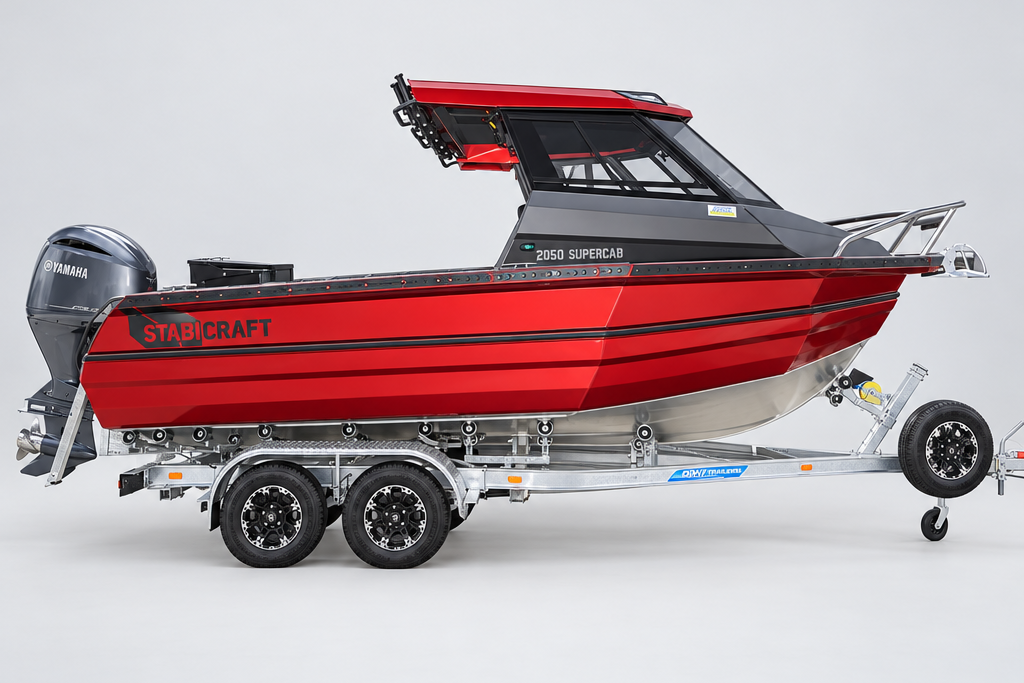 A red and gray Stabcraft motorboat on a dual-axle trailer, parked outdoors in front of a white building.
